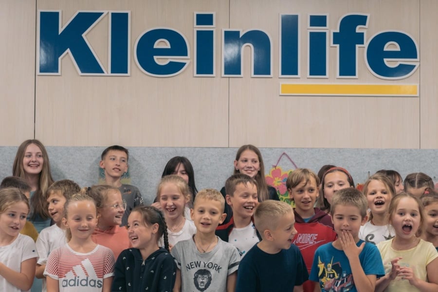 Un grupo de niñas y niños refugiados debajo de un letrero que dice Kleinlife