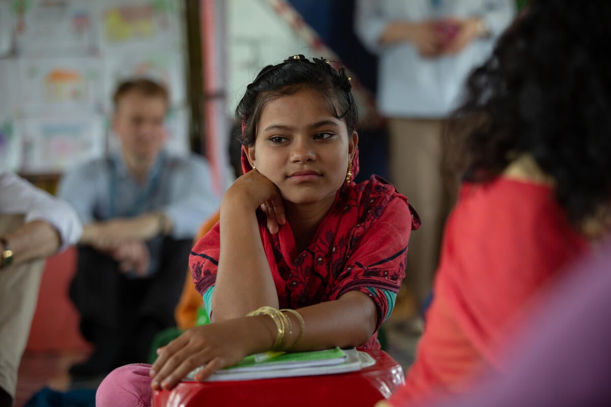 A girl dressed in red looks away from the camera while leaning on a small pile of books A girl dressed in red looks away from the camera while leaning on a small pile of books