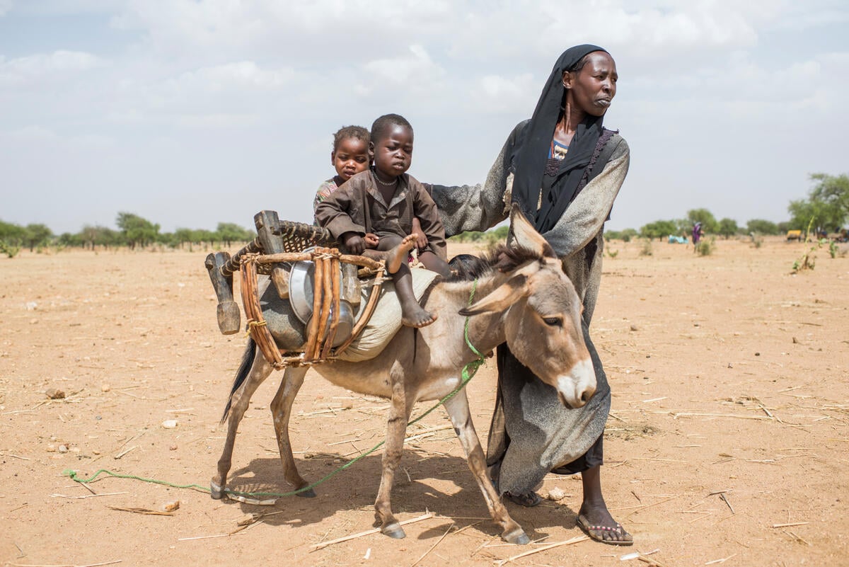 Ashta, 32, fled Tindelti, in the Darfur region of Sudan with her husband and six children. A woman walking beside a donkey, on which two children are sitting