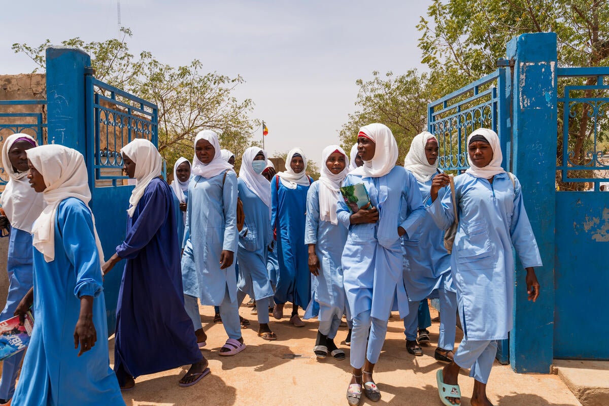 Female high school students carrying books and bags walk through school gates.