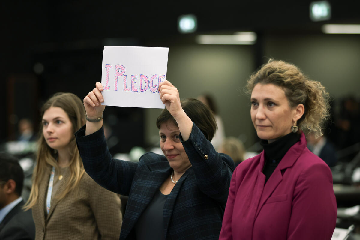 Person with a sign reading 'I pledge' Three individuals stand together, one holds up a sign that reads 'I pledge'.
