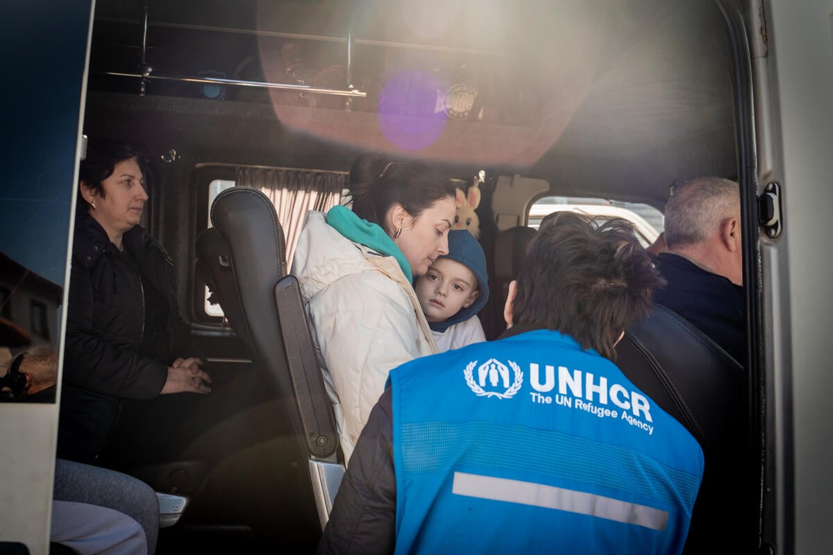 Refugees fleeing Ukraine cross the border from Slovenia into Italy. A UNHCR staff member speaks with a Ukrainian refugee mother and young boy on a bus.