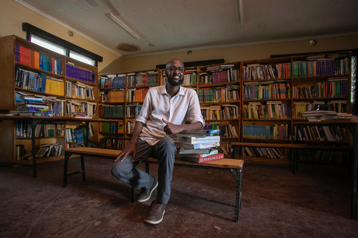 A man sits in a library, surrounded by books and leaning on a pile of books A man sits in a library, surrounded by books and leaning on a pile of books